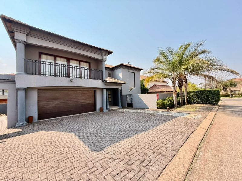 Front elevation of a modern double-story house featuring a paved driveway, double garage, and an upper-level balcony with metal railings.