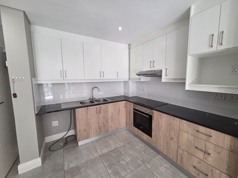 Modern kitchen featuring two-tone cabinetry, dark laminate countertops, subway tile backsplash, and integrated appliances including an oven and hob.
