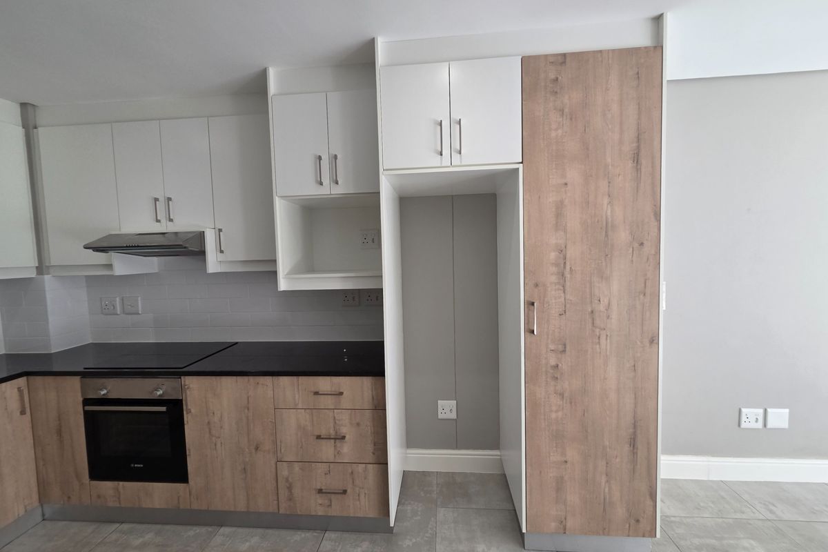 Modern kitchen featuring two-tone cabinetry, built-in oven, electric hob, extractor fan, and dedicated space for a refrigerator, finished with neutral floor tiles.