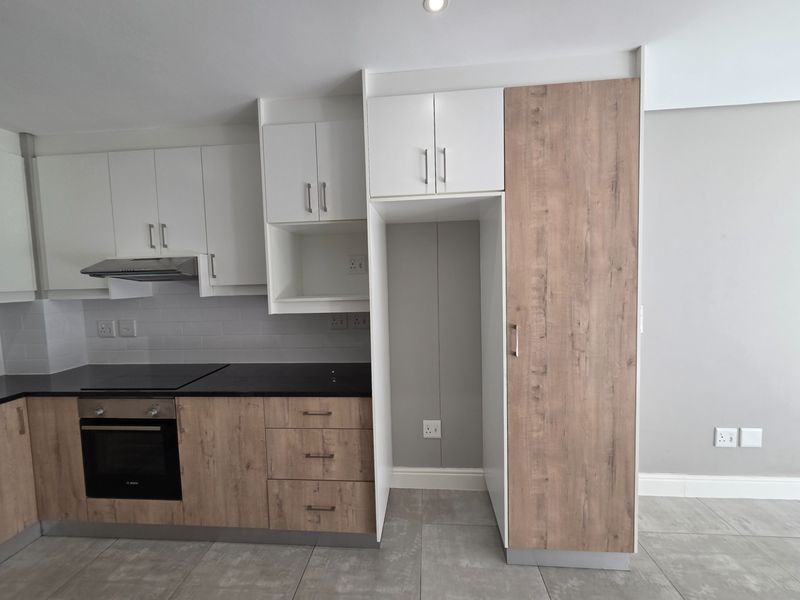 Modern kitchen featuring two-tone cabinetry, built-in oven, electric hob, extractor fan, and dedicated space for a refrigerator, finished with neutral floor tiles.