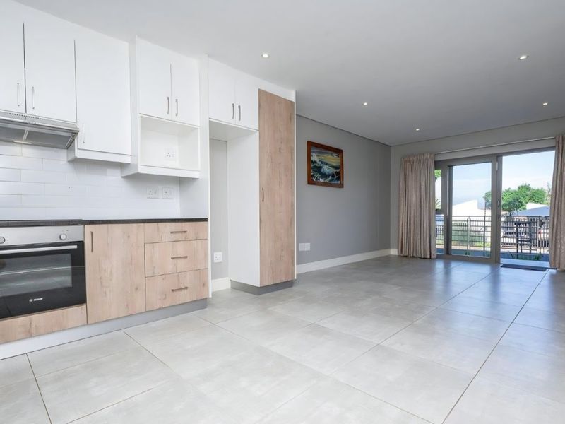 Modern open-plan kitchen and living area featuring light wood-tone cabinetry, built-in oven, tiled floors, and direct access to a private balcony.