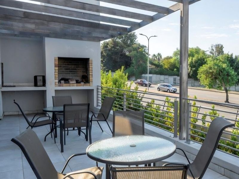 A spacious covered balcony featuring a built-in braai, timber pergola structure, and metal balustrade, offering an ideal outdoor entertainment area.