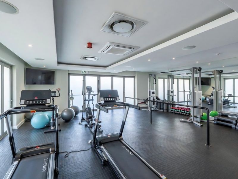 A well-equipped retirement village gym featuring rubberized flooring, mirrored walls, integrated air conditioning, and sliding glass doors providing natural light.