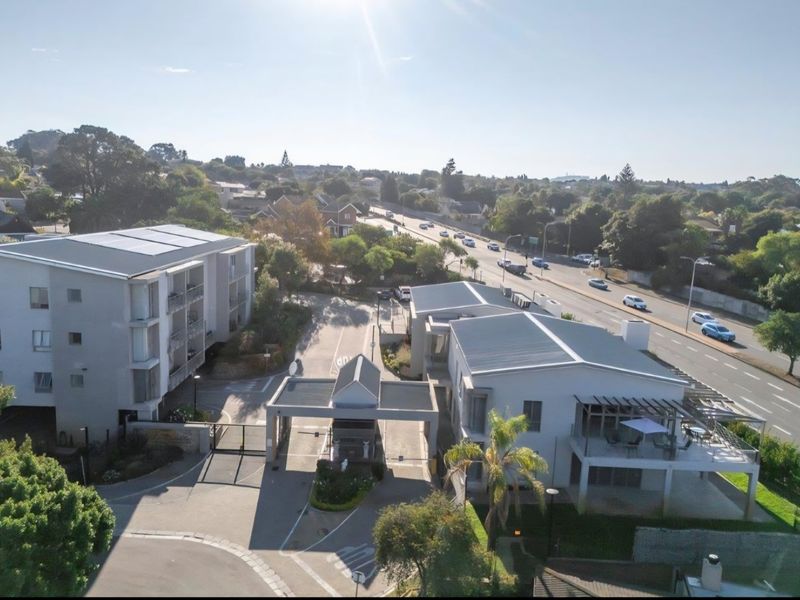 Aerial view of the retirement village complex, featuring a secure gated entrance, paved driveway, and multi-story residential buildings with solar panels.