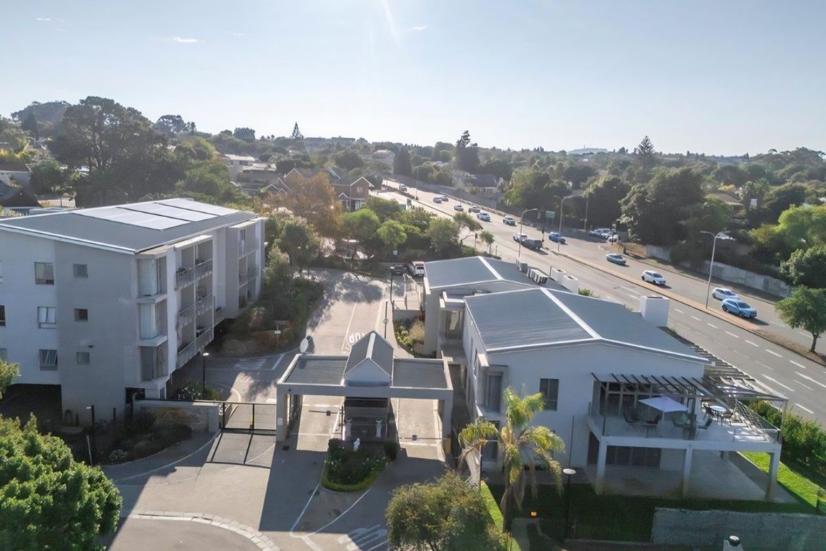 Aerial view of the retirement village complex, featuring a secure gated entrance, paved driveway, and multi-story residential buildings with solar panels.