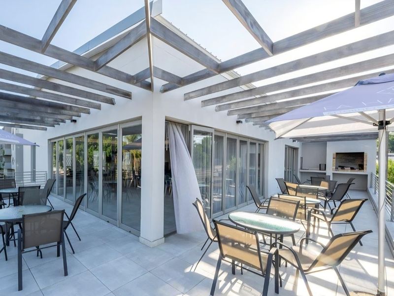 Spacious outdoor patio featuring a timber pergola, tiled flooring, and a built-in braai, seamlessly connected to the interior via large sliding glass doors.