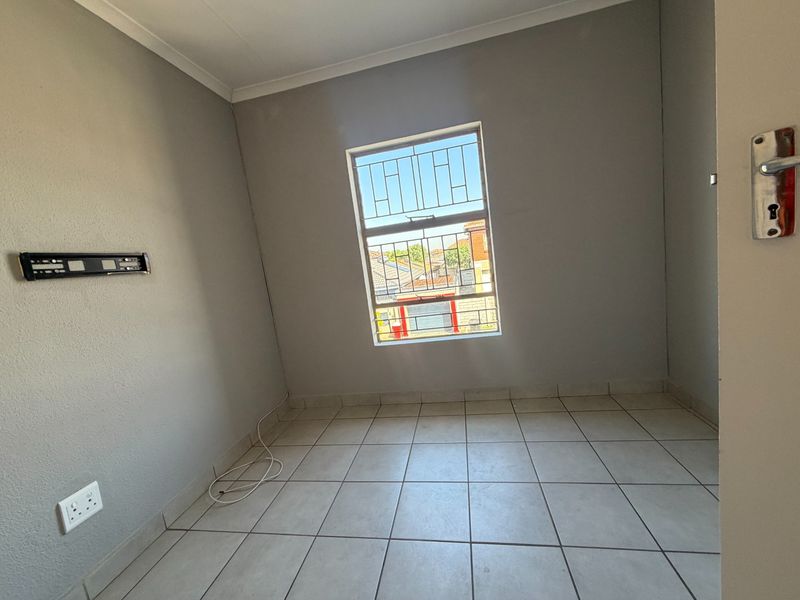 A clean, empty bedroom featuring neutral grey walls, tiled flooring, and a window fitted with security bars.