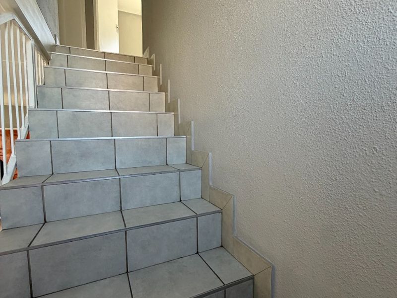A staircase featuring tiled steps and a metal balustrade leading to an upper level hallway.