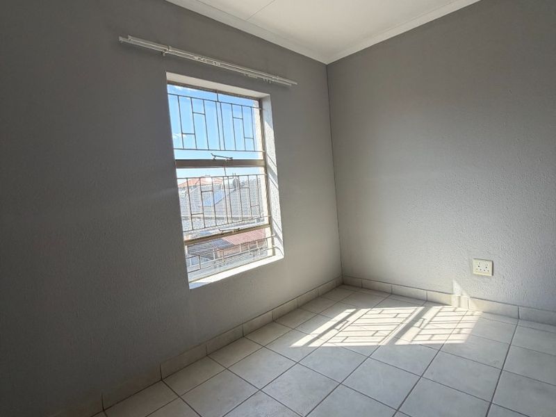 A clean, empty bedroom featuring neutral grey walls, tiled flooring, and a window fitted with security bars.