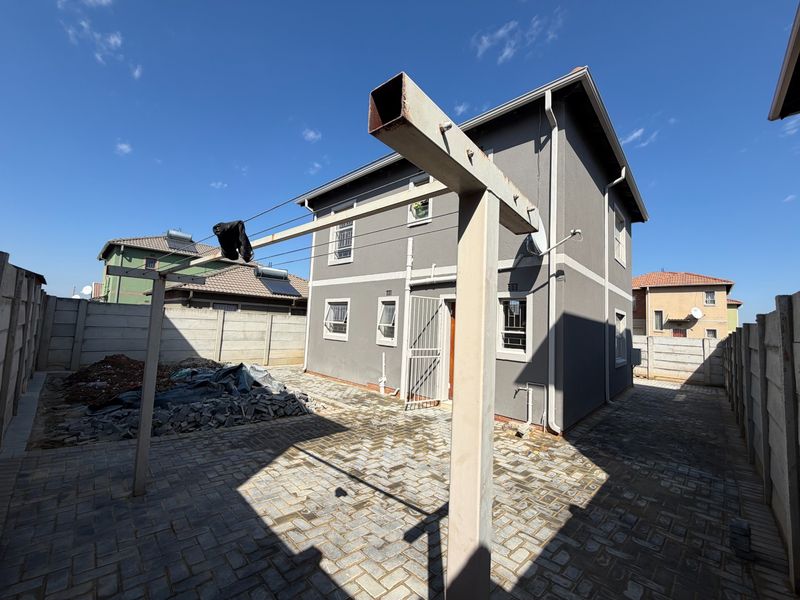Rear exterior view of a two-story house featuring a paved courtyard, precast boundary walls, and a metal washing line structure.