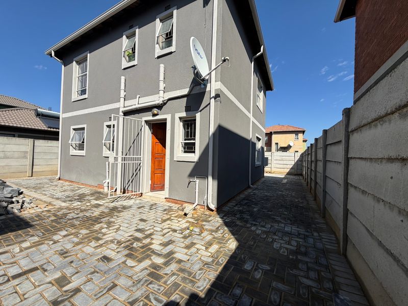 Rear exterior view of the property featuring a paved courtyard, secure entrance, and precast concrete boundary walling.