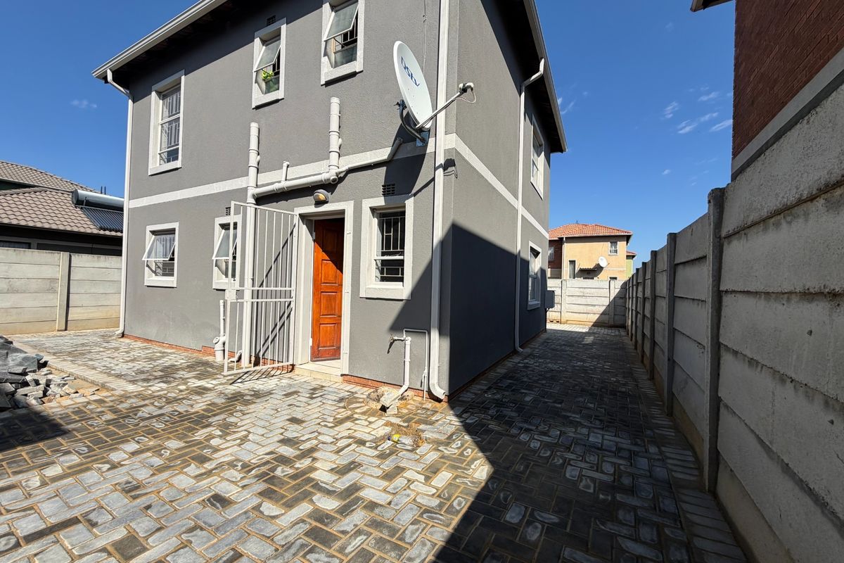 Rear exterior view of the property featuring a paved courtyard, secure entrance, and precast concrete boundary walling.