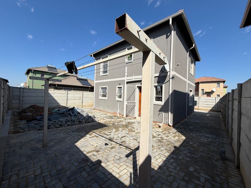 Rear exterior view of a two-story house featuring a paved courtyard, precast concrete boundary walls, and a metal washing line structure.