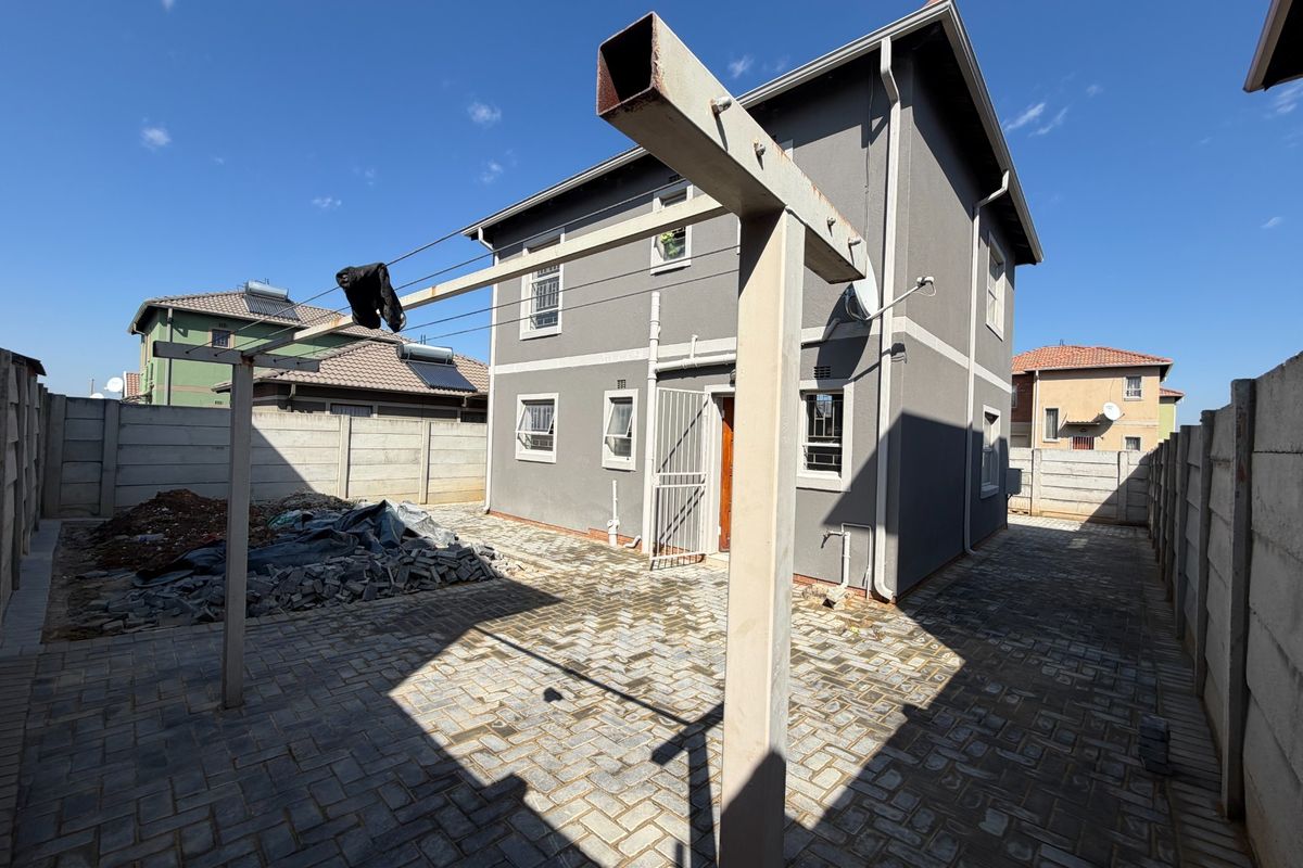Rear exterior view of a two-story house featuring a paved courtyard, precast concrete boundary walls, and a metal washing line structure.