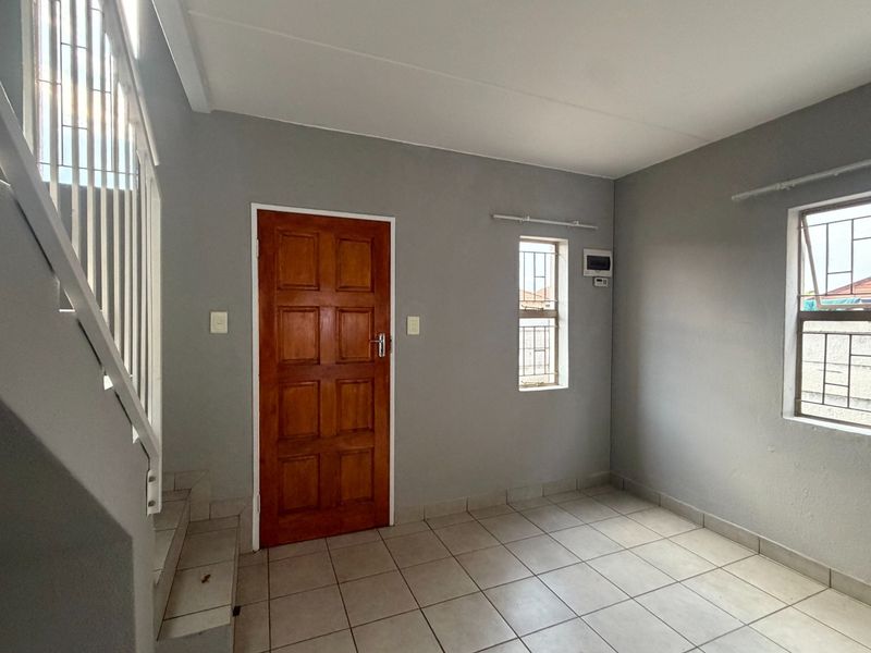 An empty entrance area featuring tiled flooring, a timber door, and an internal staircase with security bars on the windows.