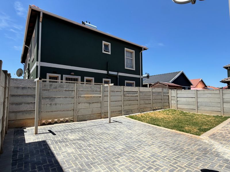 Rear exterior view featuring a paved patio area, a small lawn, and a precast concrete boundary wall against the side of the house.