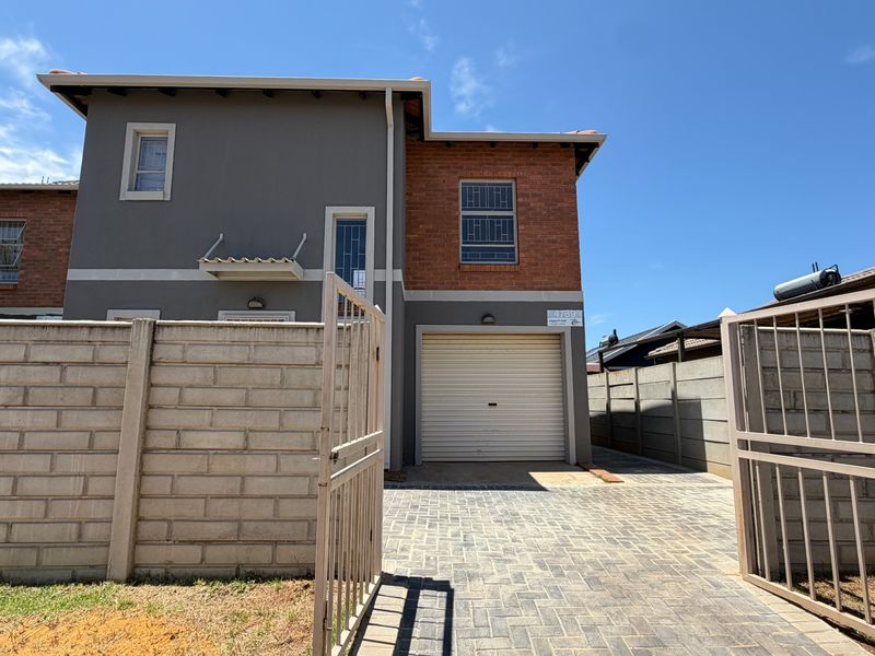 Front elevation of a two-story residential house featuring a paved driveway, roller garage door, and secure boundary walling.