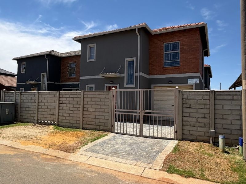 Front exterior view of a modern two-story house featuring a brick and plaster facade, tiled roof, paved driveway, and secure metal gate.