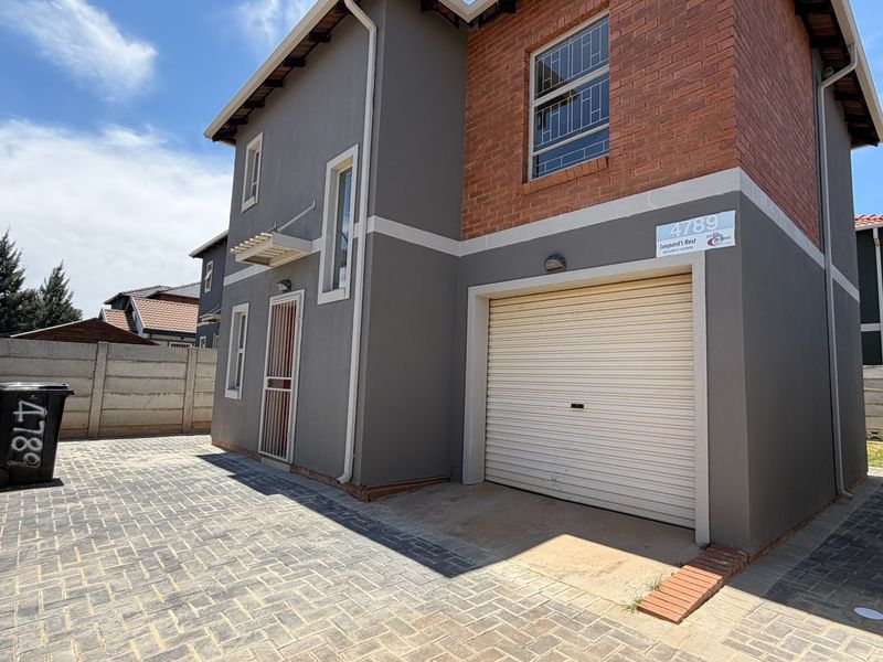 Front exterior view of a two-story residential house featuring a paved driveway, single roller garage door, and a combination of brick and plastered wall finishes.