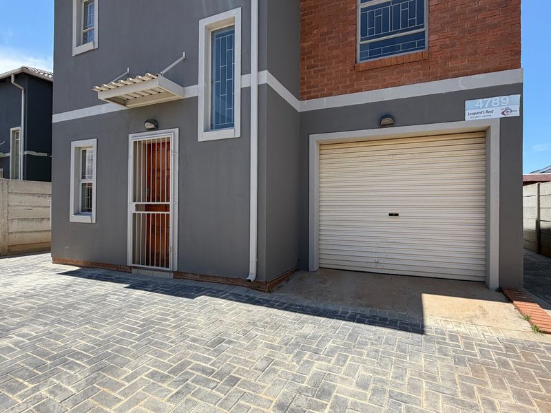 Front elevation of a modern two-story house featuring a paved driveway, integrated garage with roller door, and secure entrance.