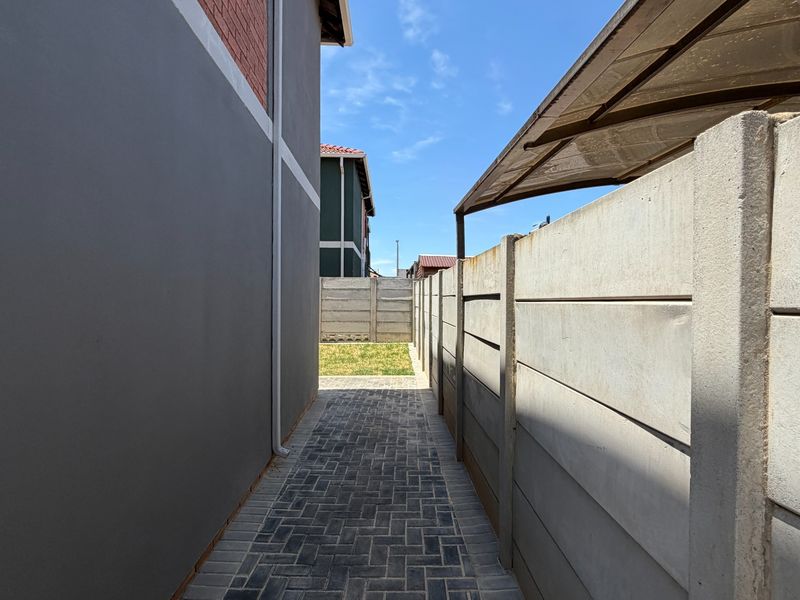 A side passage featuring a paved walkway, precast concrete boundary wall, and a small section of lawn at the rear.