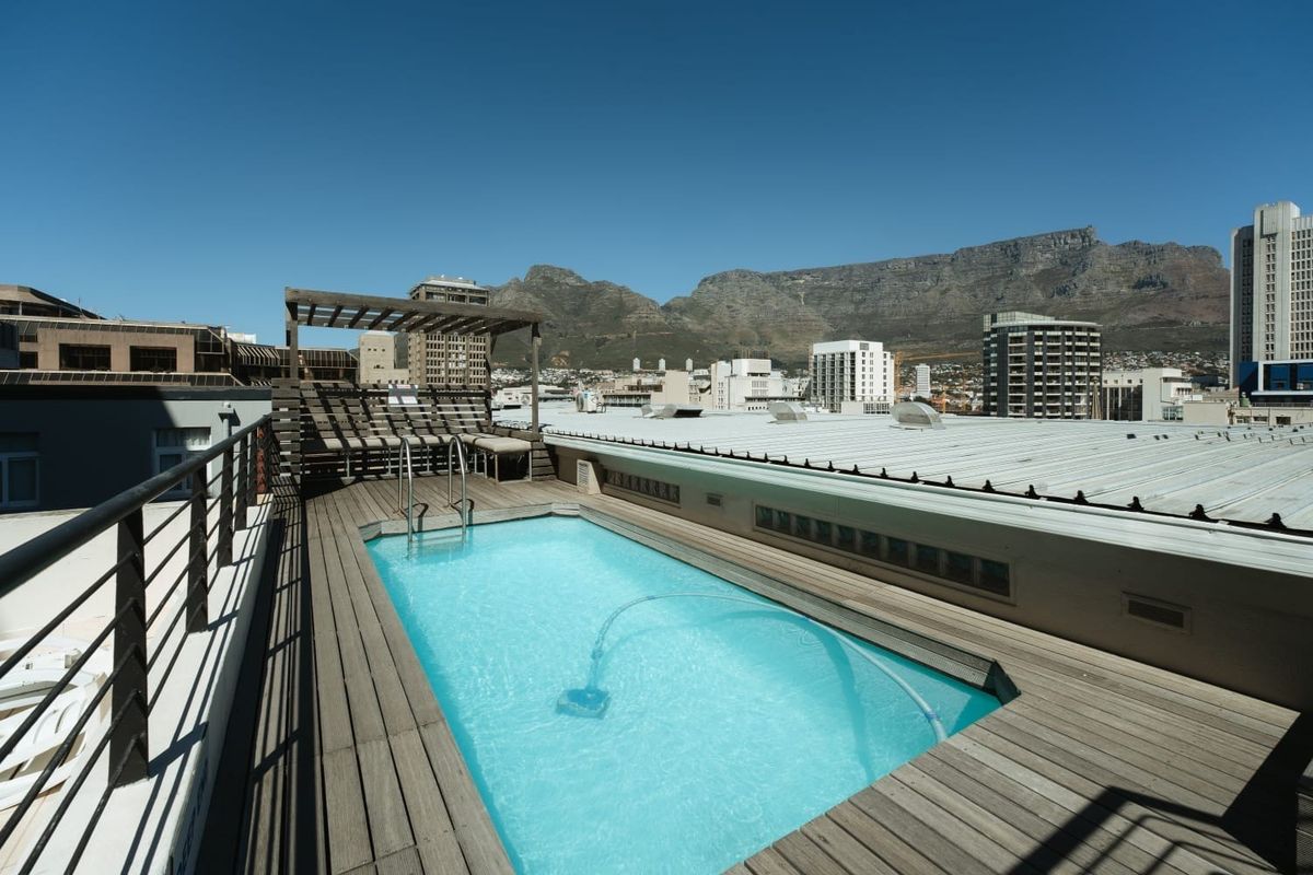 Rooftop swimming pool featuring timber decking, a pergola, and panoramic mountain and city views.