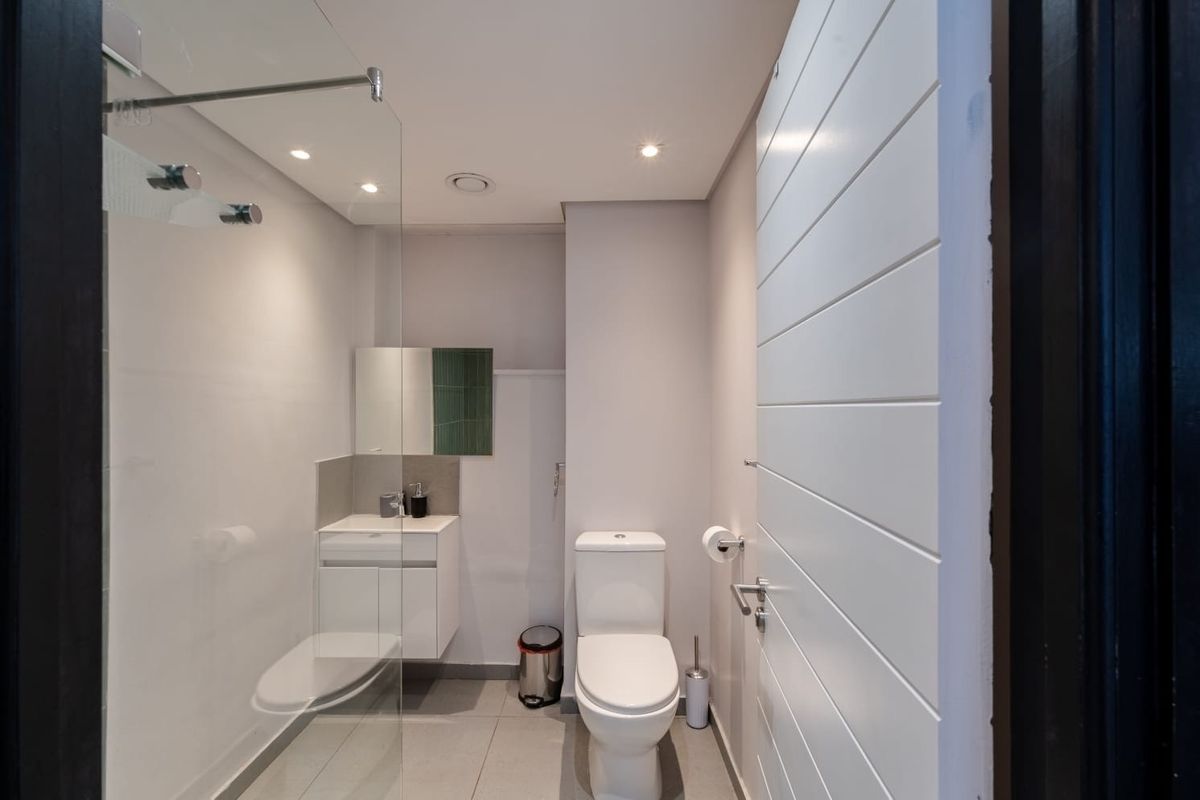 A modern, compact bathroom featuring a glass-enclosed shower, wall-mounted vanity, and contemporary toilet with neutral tiled flooring and recessed lighting.