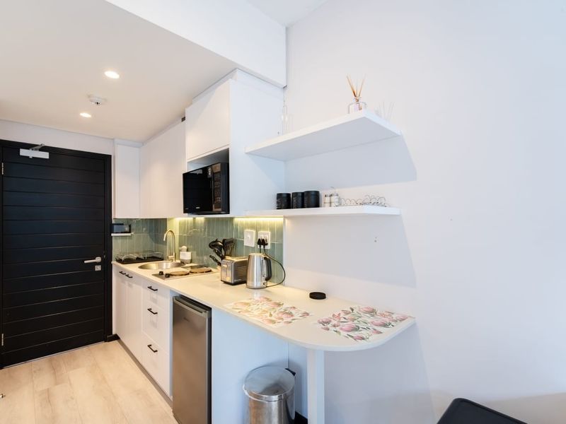 Modern compact kitchen featuring white cabinetry, integrated microwave, hob, sink, and stylish green tiled splashback with under-cabinet lighting.