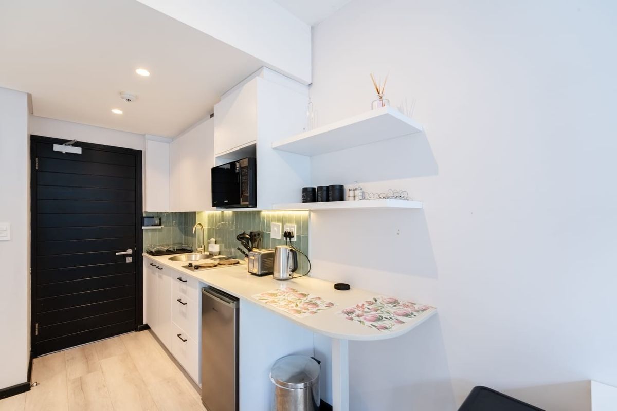 Modern compact kitchen featuring white cabinetry, integrated microwave, hob, sink, and stylish green tiled splashback with under-cabinet lighting.