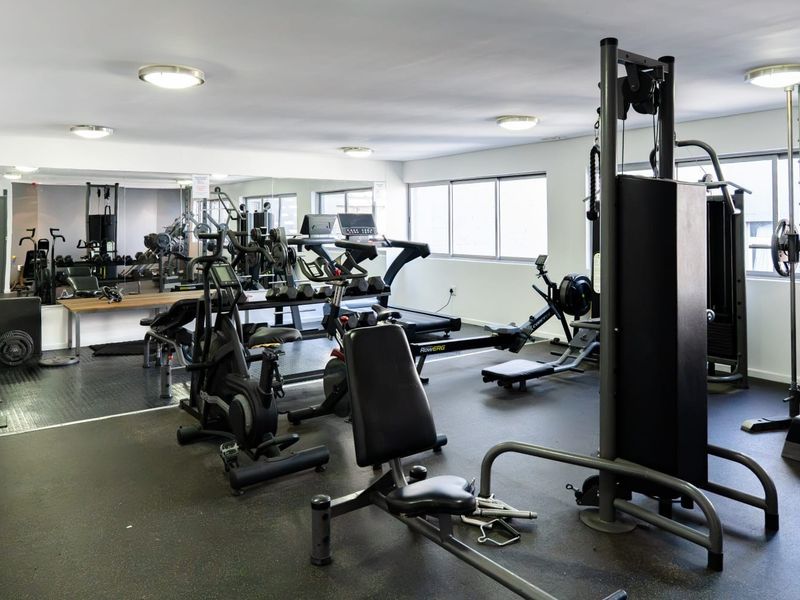 A well-equipped home gym featuring mirrored walls, durable rubberized flooring, and recessed ceiling lighting, providing a functional space for fitness activities.