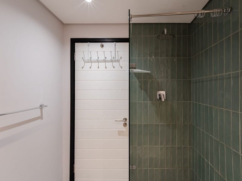 A modern bathroom featuring a walk-in shower with green subway-style wall tiles, a glass screen, and a sleek chrome shower mixer.