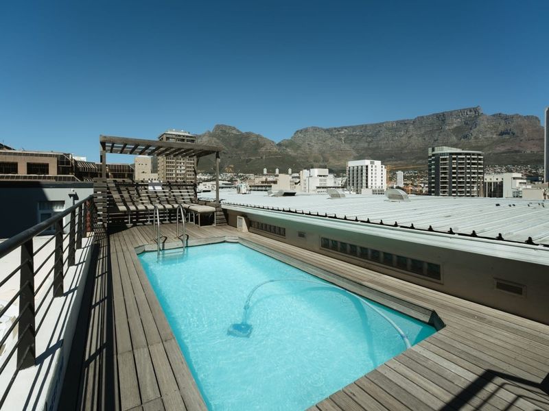Rooftop swimming pool featuring timber decking, a pergola, and panoramic mountain and city views.