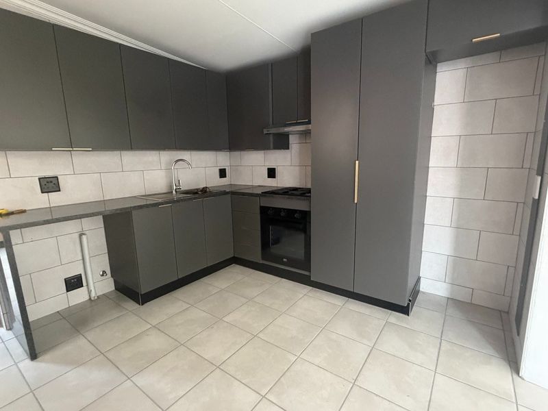 Modern kitchen featuring dark grey cabinetry, stone countertops, built-in oven, hob, extractor fan, and neutral tiled flooring.