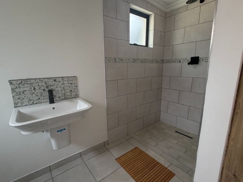 Modern bathroom featuring a wall-mounted basin with black fixtures and a spacious walk-in shower with contemporary grey tiling and a linear drain.