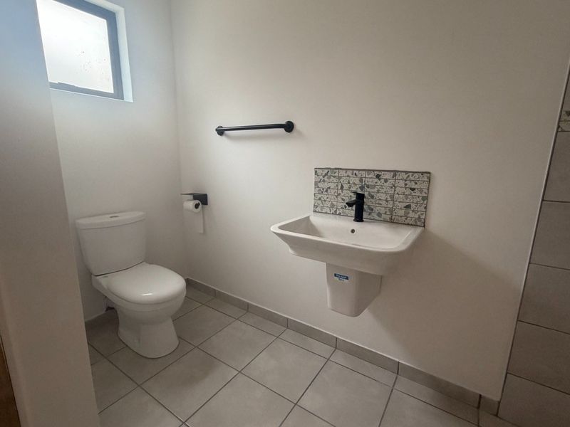 A clean and modern guest bathroom featuring a wall-mounted basin with a decorative tiled splashback, a toilet, and neutral floor tiles.
