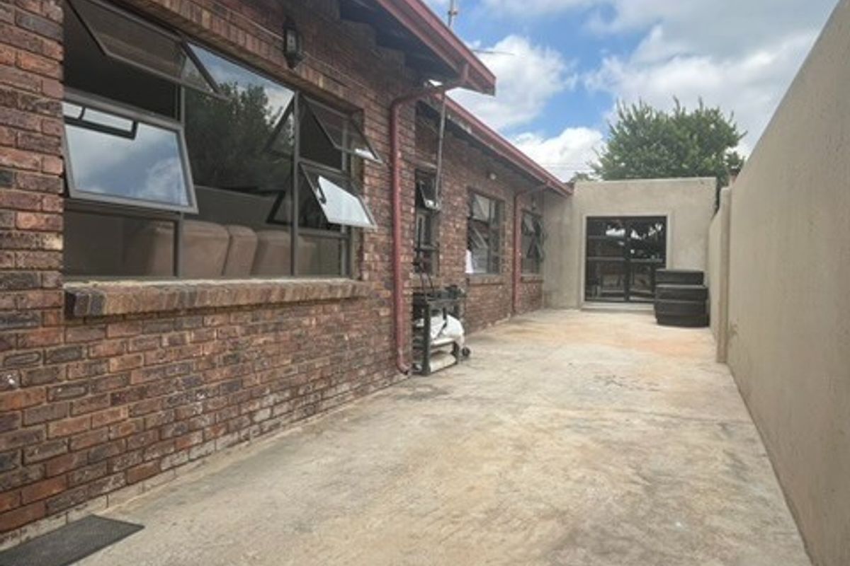 Rear exterior view of the apartment featuring a brick facade, concrete paved area, and boundary wall, providing a functional outdoor space.