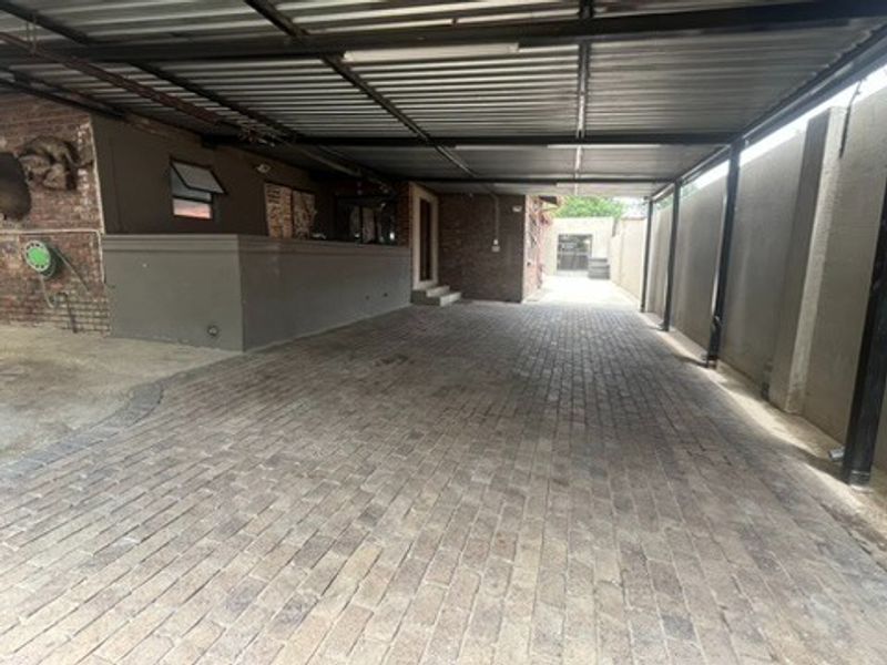 A spacious covered parking area featuring durable brick paving and a sturdy metal roof structure, providing ample space for vehicles.
