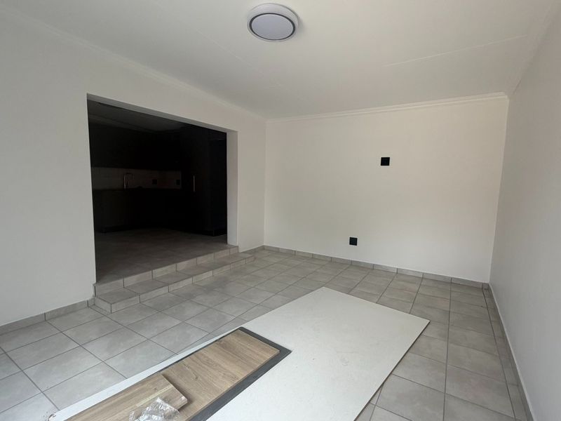 An empty living room area featuring neutral tiled flooring, a raised step transition, and a flush mount ceiling light fixture.