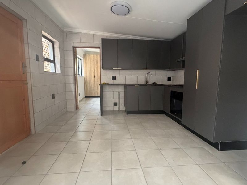 A modern, empty kitchen featuring dark grey cabinetry, tiled flooring, a built-in oven, and a tiled backsplash, offering a clean and functional workspace.