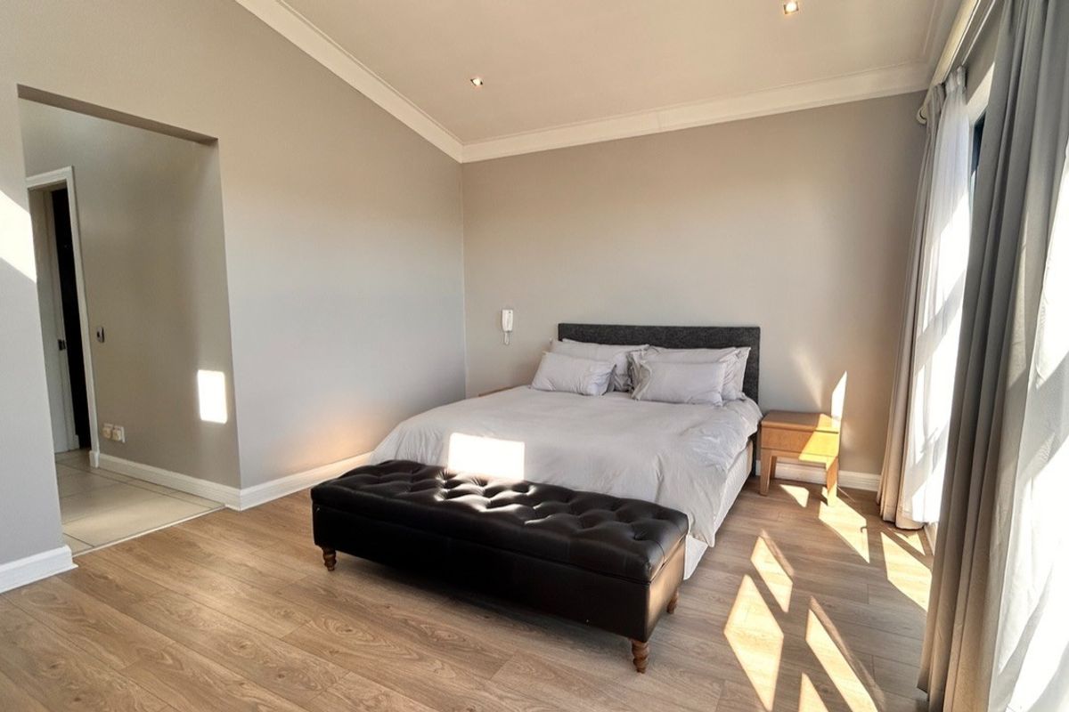 A well-maintained bedroom featuring modern laminate flooring, recessed downlighting, and neutral wall finishes with access to an adjoining space.