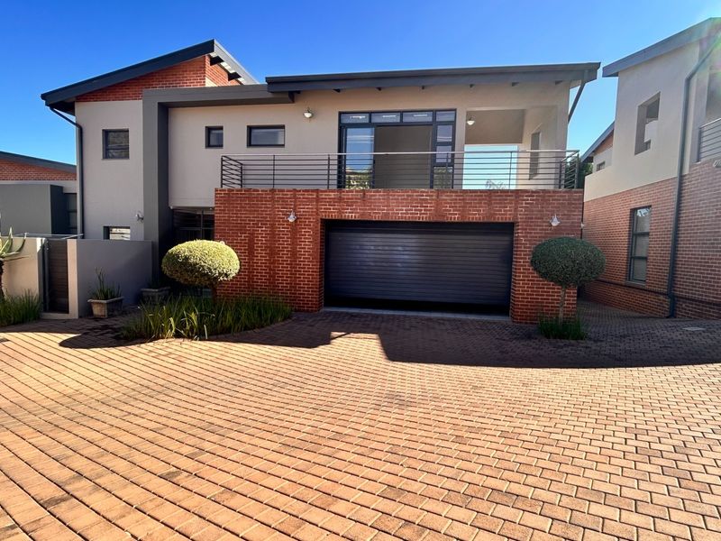 Modern double-story residence featuring a brick facade, an integrated automated garage, and an upper-level balcony with metal railings, set on a paved driveway.
