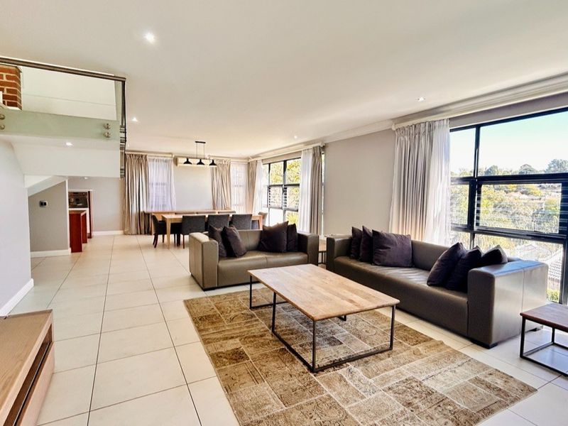 Spacious open-plan living and dining area featuring large windows, tiled flooring, and a modern glass balustrade staircase.