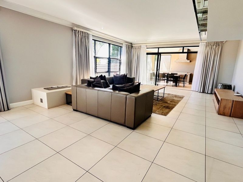 Spacious open-plan living area featuring large format floor tiles, recessed lighting, and seamless flow to an outdoor patio through sliding glass doors.