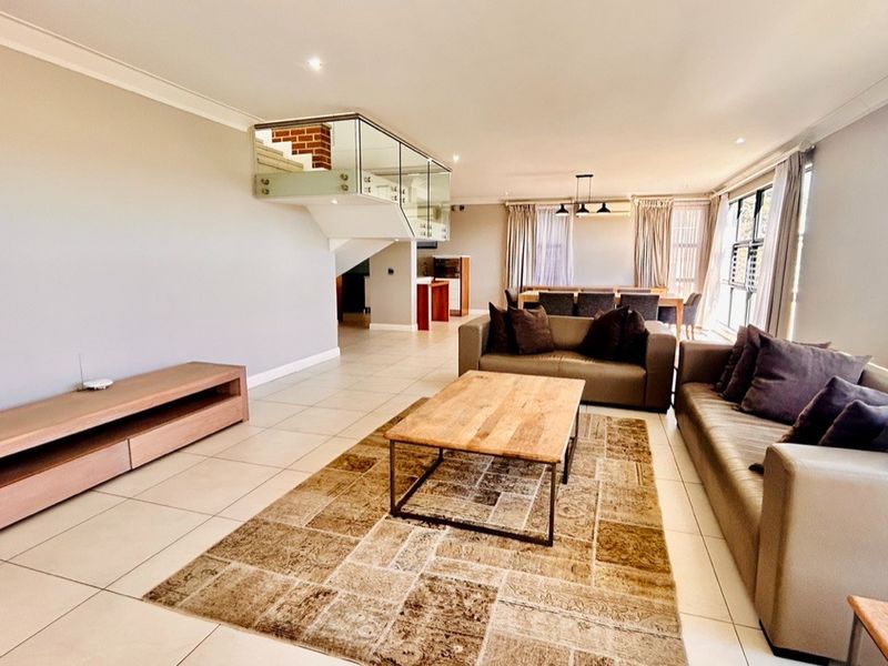 Spacious open-plan living and dining area featuring tiled flooring, modern glass balustrade staircase, and recessed lighting, creating a bright and airy atmosphere.