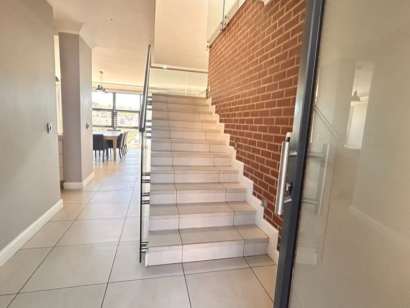 Modern entrance hallway featuring a tiled staircase with a glass balustrade, an exposed brick feature wall, and large format floor tiles.