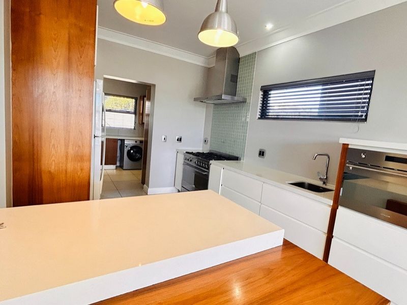 Modern kitchen featuring sleek white cabinetry, stone countertops, stainless steel appliances, and a gas hob, with an adjacent scullery area.
