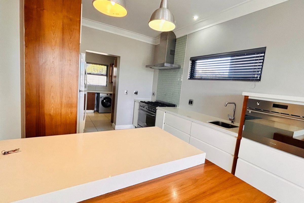 Modern kitchen featuring sleek white cabinetry, stone countertops, stainless steel appliances, and a gas hob, with an adjacent scullery area.