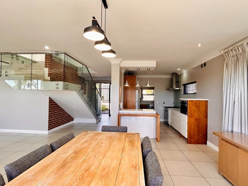 Spacious open-plan living and kitchen area featuring a modern staircase with glass balustrade, exposed brickwork, and contemporary kitchen cabinetry.