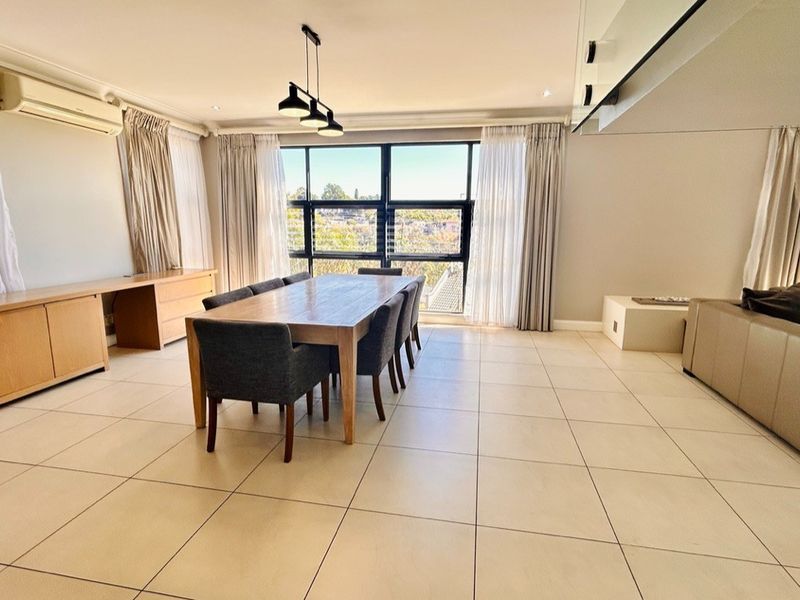 Spacious open-plan living and dining area featuring large windows, tiled flooring, modern pendant lighting, and integrated air conditioning.