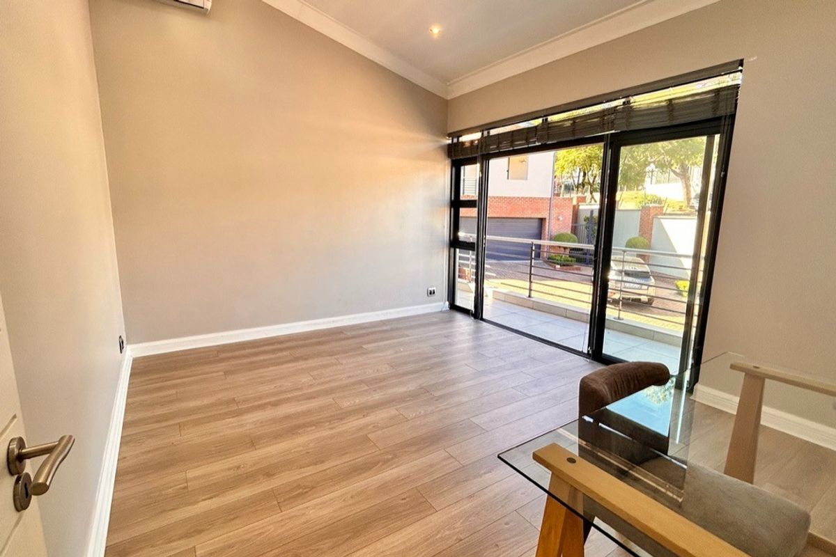 A bright, empty living room featuring modern laminate flooring, high ceilings, and large sliding glass doors that open onto a balcony.